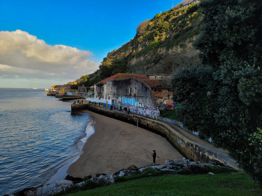 A serene riverside garden, Jardim do Rio, in Cacilhas, Almada, Portugal, featuring lush greenery, walking paths, and breathtaking views of the Tagus River and Lisbon skyline. The peaceful atmosphere makes it a perfect spot for relaxation and sightseeing.